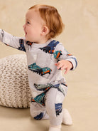 Baby crawling in a long sleeve romper with an all-over vintage steam locomotive train print, viewed from the side.