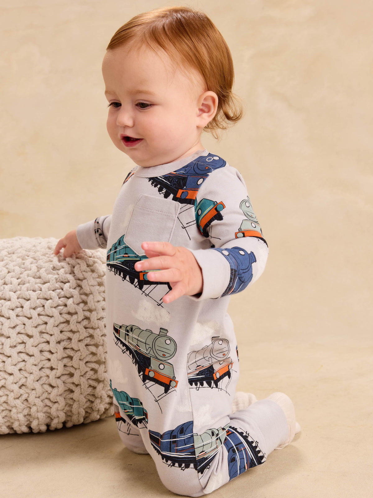 Baby crawling in a long sleeve romper with an all-over vintage steam locomotive train print, viewed from the side.