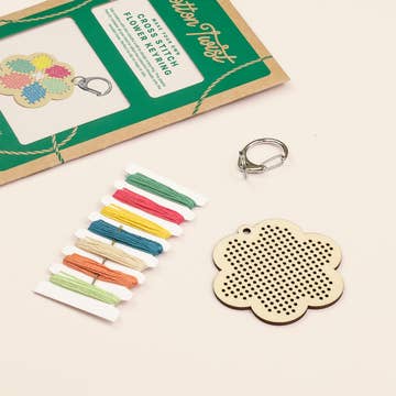 Cross-stitch flower keyring kit with colorful threads and wooden keychain on a white background
