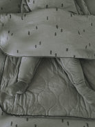 A close-up of a baby sleeping in a matching sage green quilted blanket and footed sleeper set with a small embroidered tree pattern.
