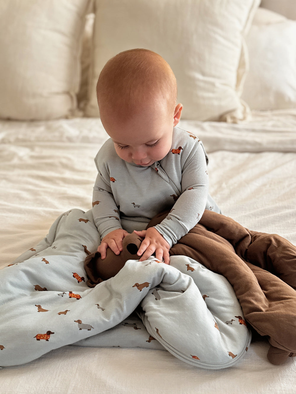 Baby sitting on a bed with a gray blanket and brown pants