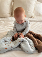 Baby sitting on a bed with a gray blanket and brown pants