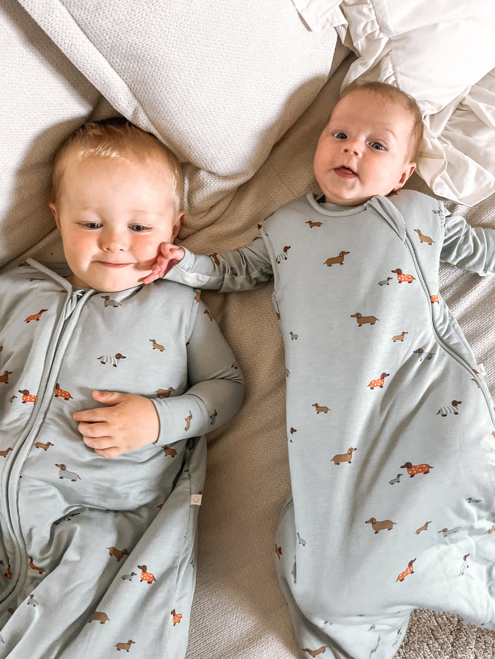 Two babies wearing matching pajamas with dog patterns lying on a bed.