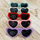 Set of heart-shaped sunglasses in various colors on a wooden surface
