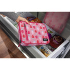Pink strawberry-patterned pouch held over an open refrigerator door.