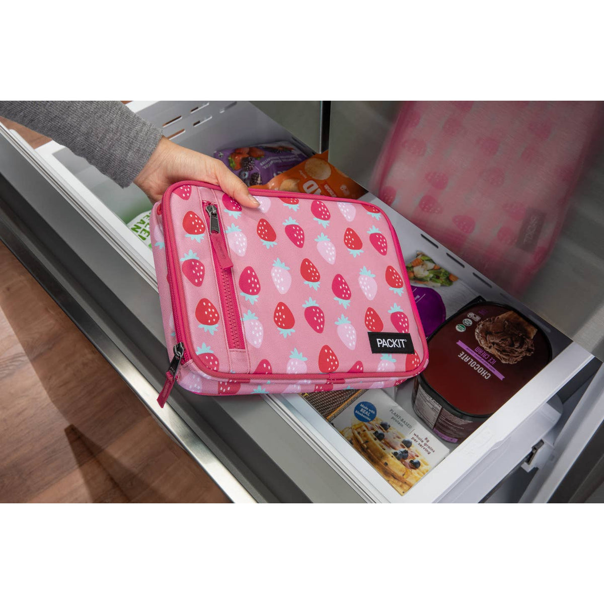 Pink strawberry-patterned pouch held over an open refrigerator door.