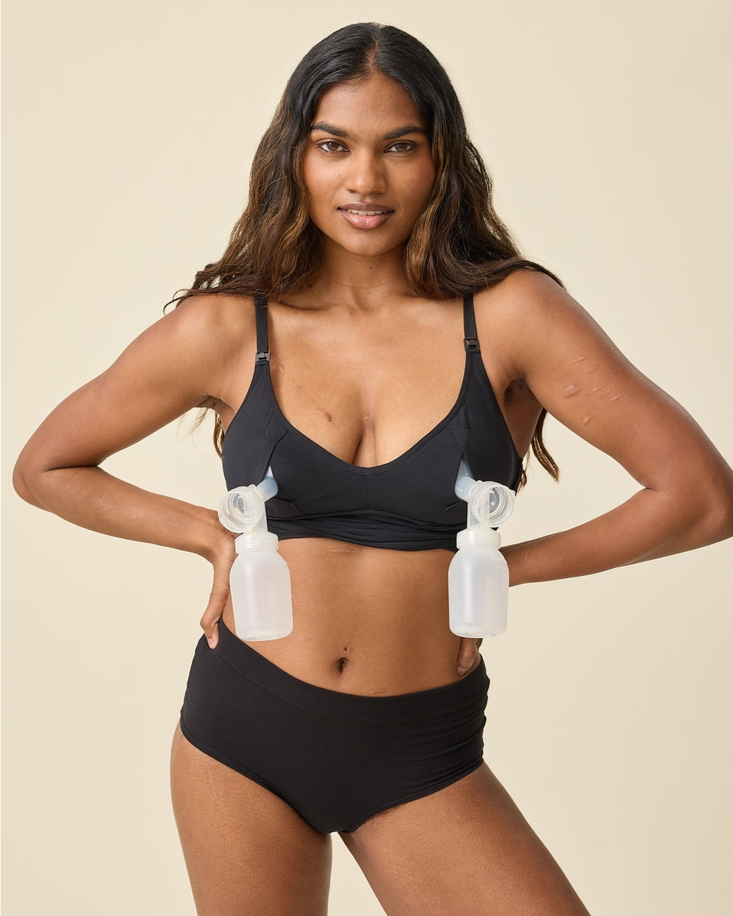 Woman wearing a black bikini holding two bottles against a beige background