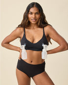 Woman wearing a black bikini holding two bottles against a beige background