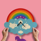 Children's clock with rainbow and cloud design on a pink background