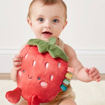 Baby holding a plush strawberry toy against a plain background