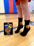 Person wearing black socks with basketball designs on a gym floor, next to a packaging of Living Royal socks.