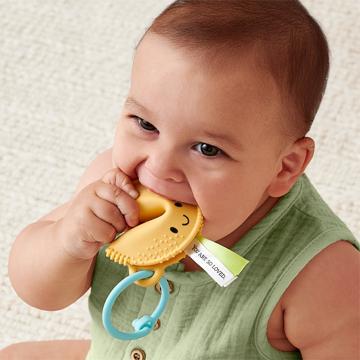 Baby holding a yellow teething toy with a smiley face