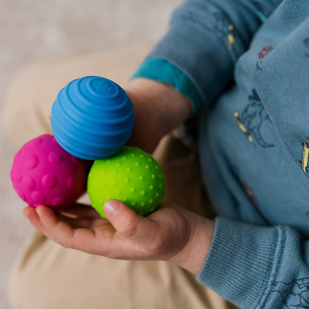 Child holding three colorful textured balls in their hands