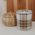 Candle with plaid design next to a pumpkin on a neutral background