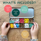 Open tin with wooden beads and accessories on a wooden surface, showing what's included.