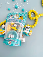 Bubble Buddies Mini KidDough Play Pack toy set in a clear plastic bag with a teal and white checkered label, displayed on a light blue-gray surface with yellow pom-pom beads and small decorative figurines around it.