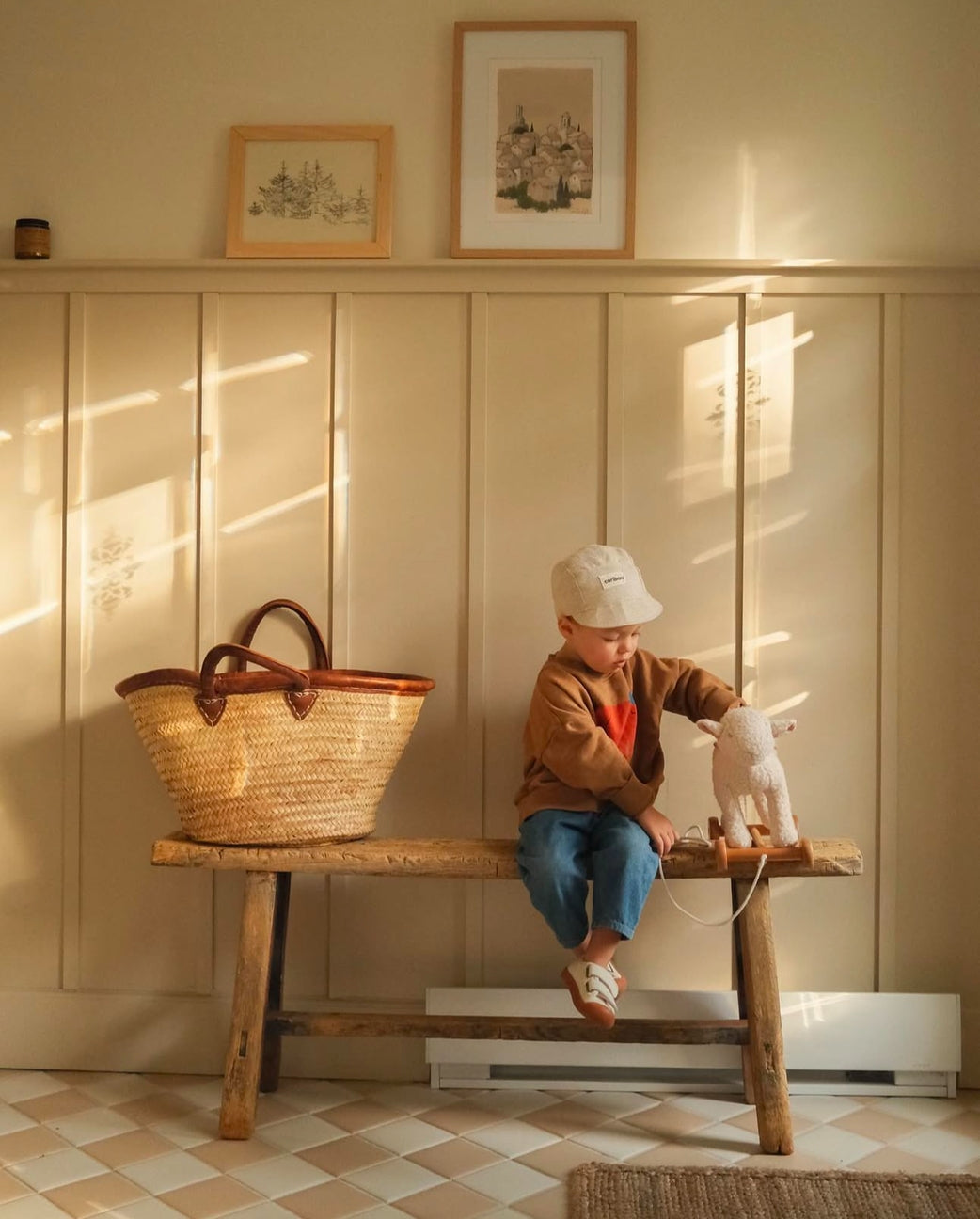 Child sitting on a wooden bench with a woven basket and toy in a warm, sunlit room.