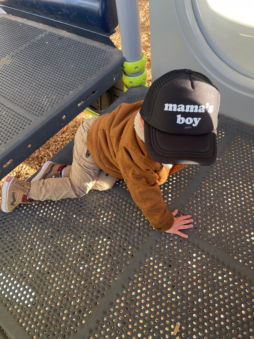 Child wearing a 'mama's boy' cap on a playground surface