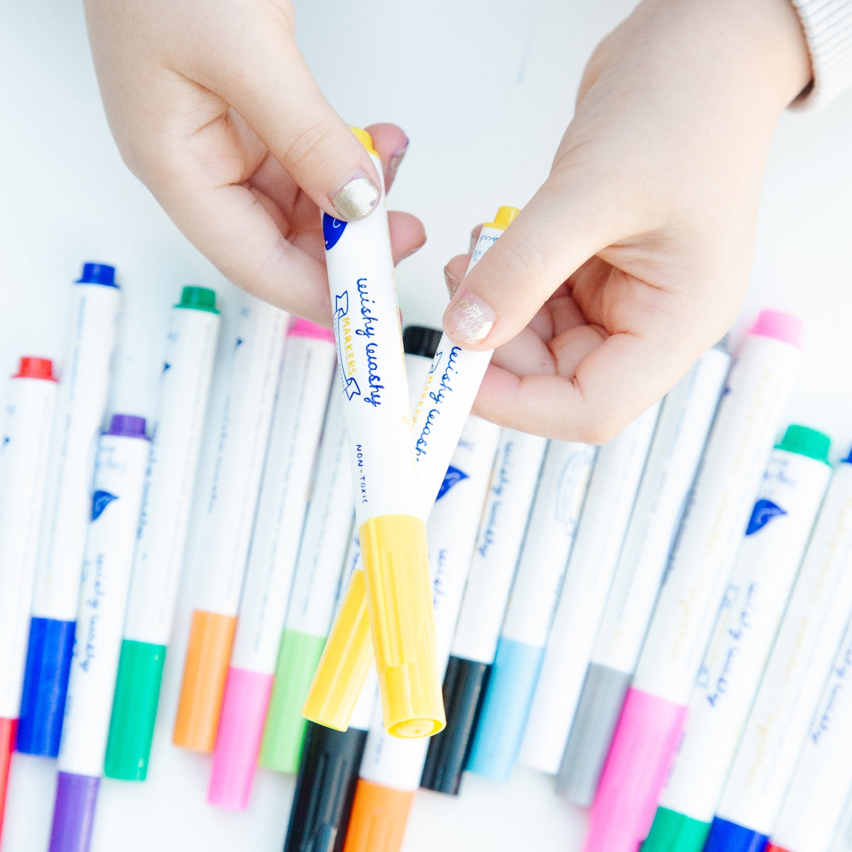 Colorful markers with a hand holding one, on a white background
