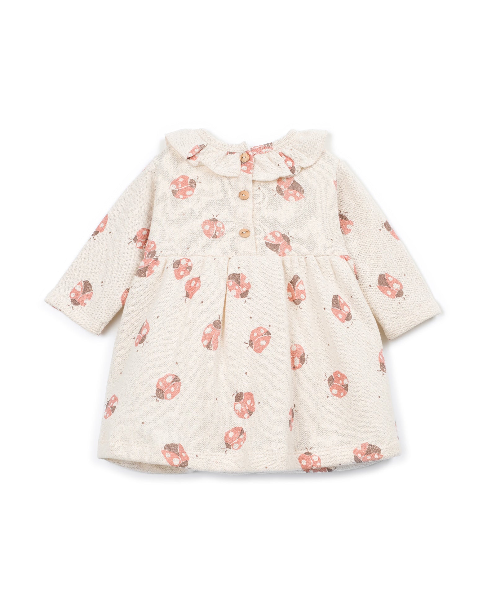 A long-sleeve baby dress in cream with a pink ladybug print, featuring a ruffled collar and button details at the chest.