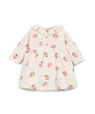 A long-sleeve baby dress in cream with a pink ladybug print, featuring a ruffled collar and button details at the chest.