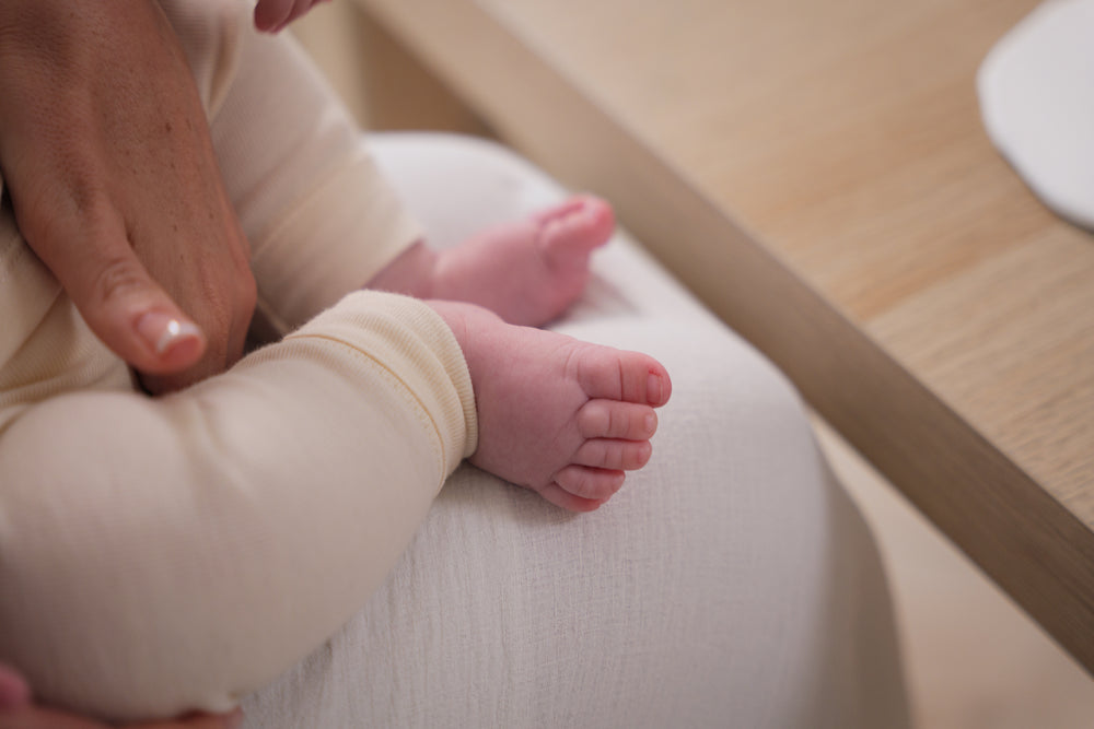 Baby's feet being held by an adult hand on a light wooden floor.