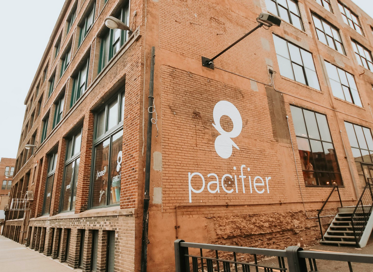 Corner View of Pacifier North Loop's exterior with a brick wall that has a white decal with the Pacifier Logo