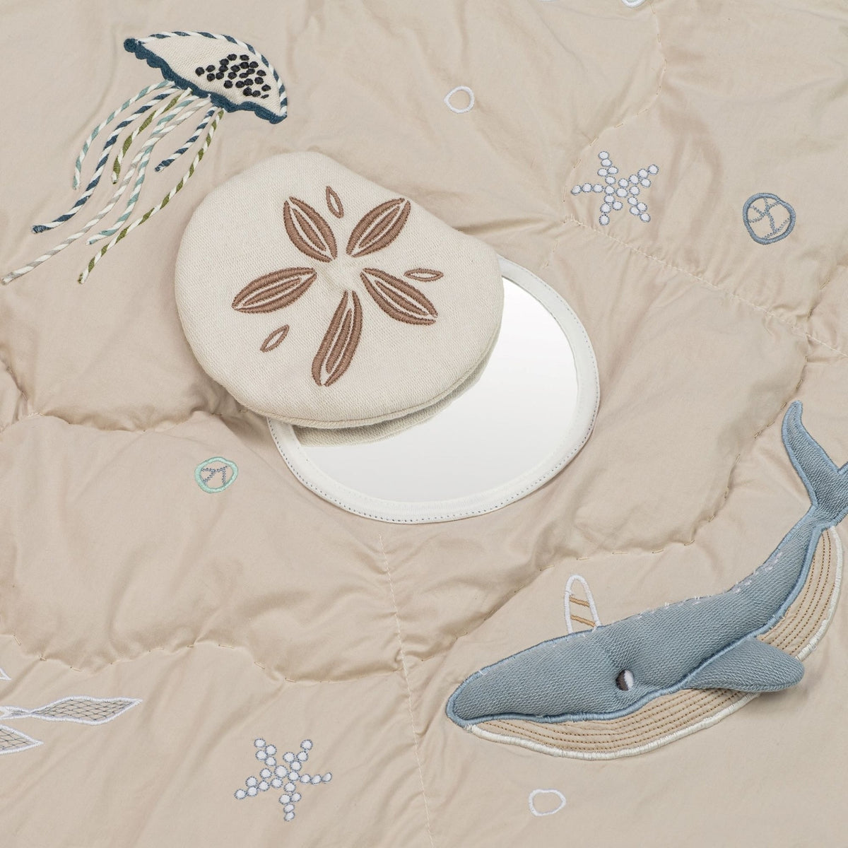 Beige quilt with embroidered sea-themed elements including a whale, jellyfish, sand dollar, and starfish.