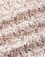 A close-up of a fabric surface with a repeating floral and leaf pattern in dusty pink and muted brown on a warm off-white background.