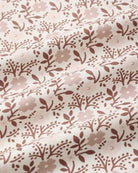 A close-up of a fabric surface with a repeating floral and leaf pattern in dusty pink and muted brown on a warm off-white background.