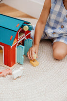 A child’s hands operating the working pulley system on the Wooden Big Red Barn Playset by Mentari, lifting a yellow magnetic hay bale toward the loft while open double doors reveal a glimpse inside the red barn.