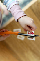 Child's hand using scissors to cut a piece of paper with a fish on it.