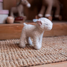 Small white plush lamb toy on a textured surface with blurred toys in the background
