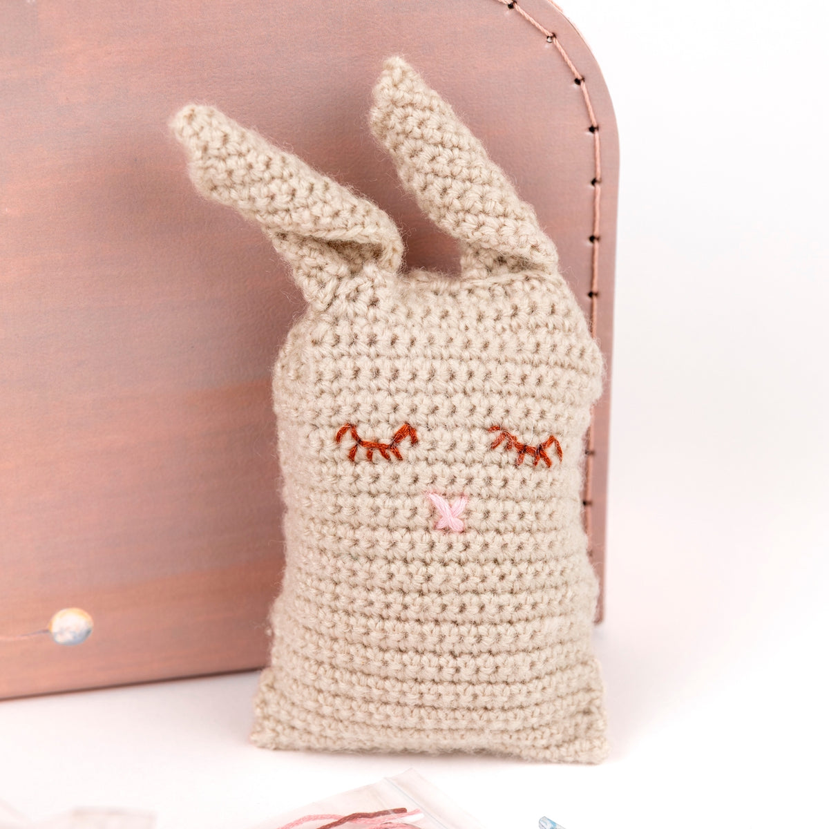 Crocheted rabbit plush toy with embroidered facial features on a pink background