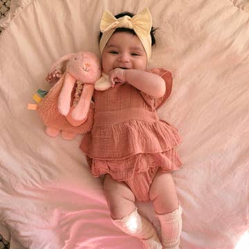 Baby in a ruffled pink outfit with a plush toy on a soft pink blanket