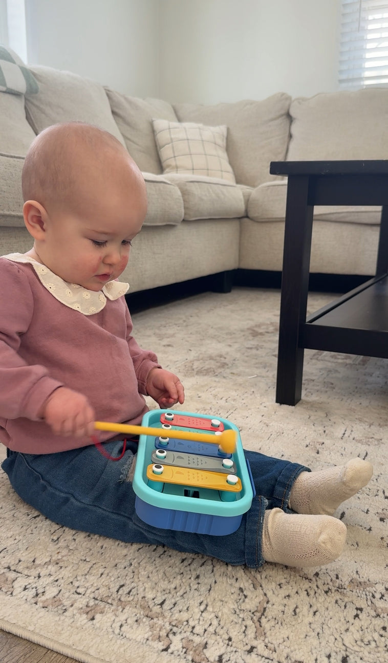 Baby playing with a colorful toy xylophone on a carpeted floor.