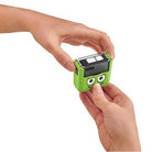 Green toy device with cartoonish face held by a person's hands on a white background