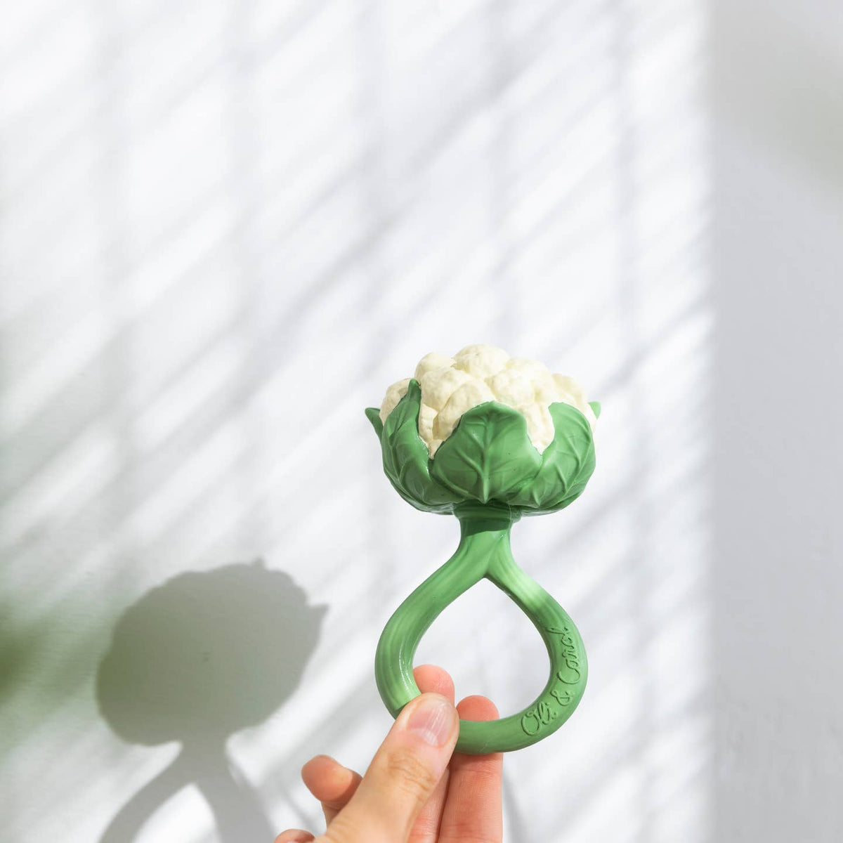 Green baby teether shaped like a flower held by a hand against a white background