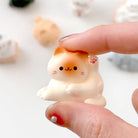 Small white dog figurine held between fingers with a blurred background