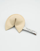 Beige fortune cookie-shaped toy with a tag on a white background