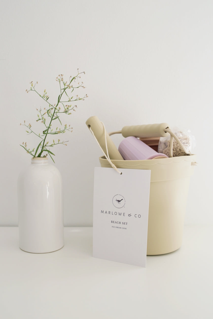 Beige basket with a pink item, white vase with greenery, and 'Marlowe & Co' tag on a light background