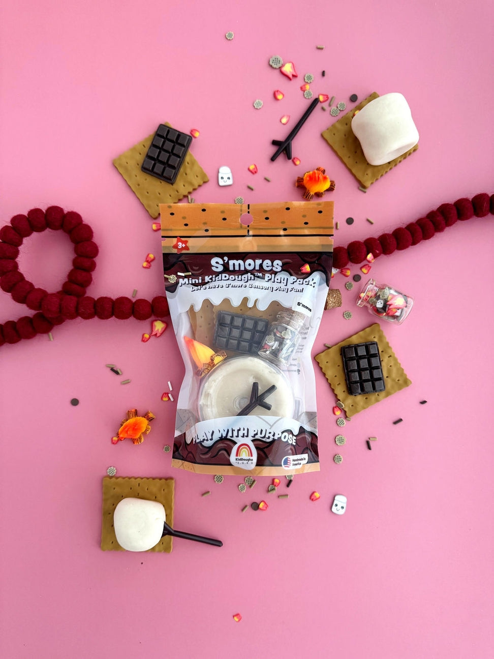 S'mores mini kit with marshmallows, graham crackers, and chocolate on a pink background