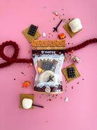 S'mores mini kit with marshmallows, graham crackers, and chocolate on a pink background