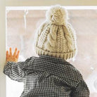Child wearing a knitted hat and checkered coat, reaching out of a window.