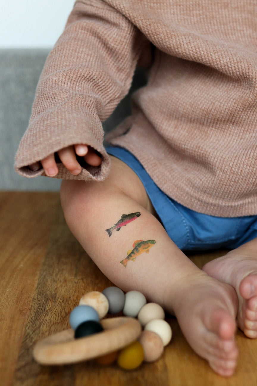 Child with temporary fish tattoos on a wooden surface