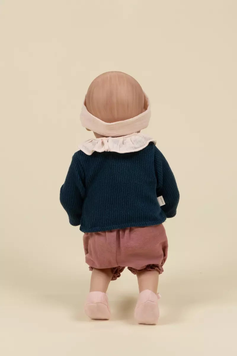 Child wearing a navy blue sweater, pink shorts, and a matching headband on a beige background
