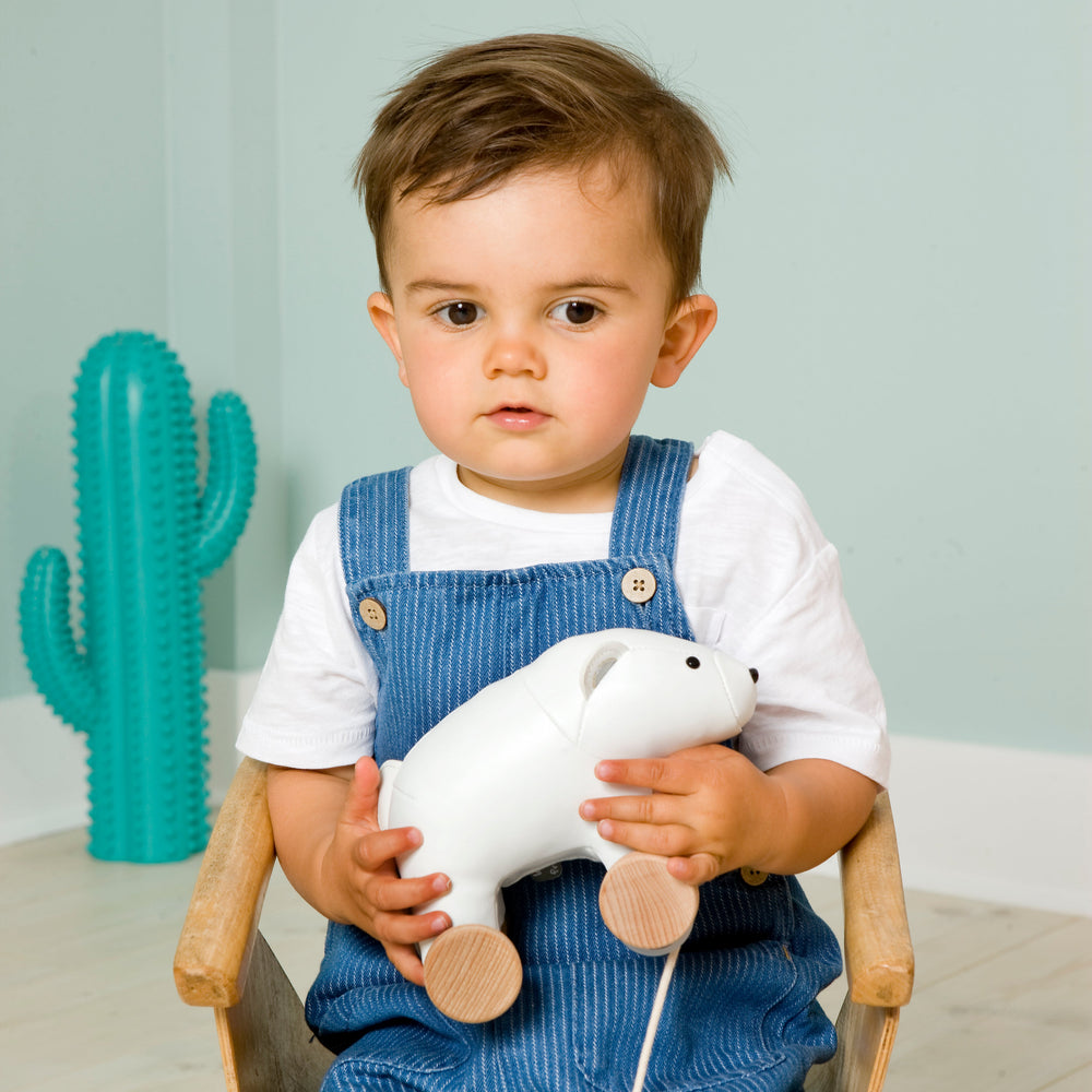 Child holding a white toy bear in a room with a green cactus-shaped object.