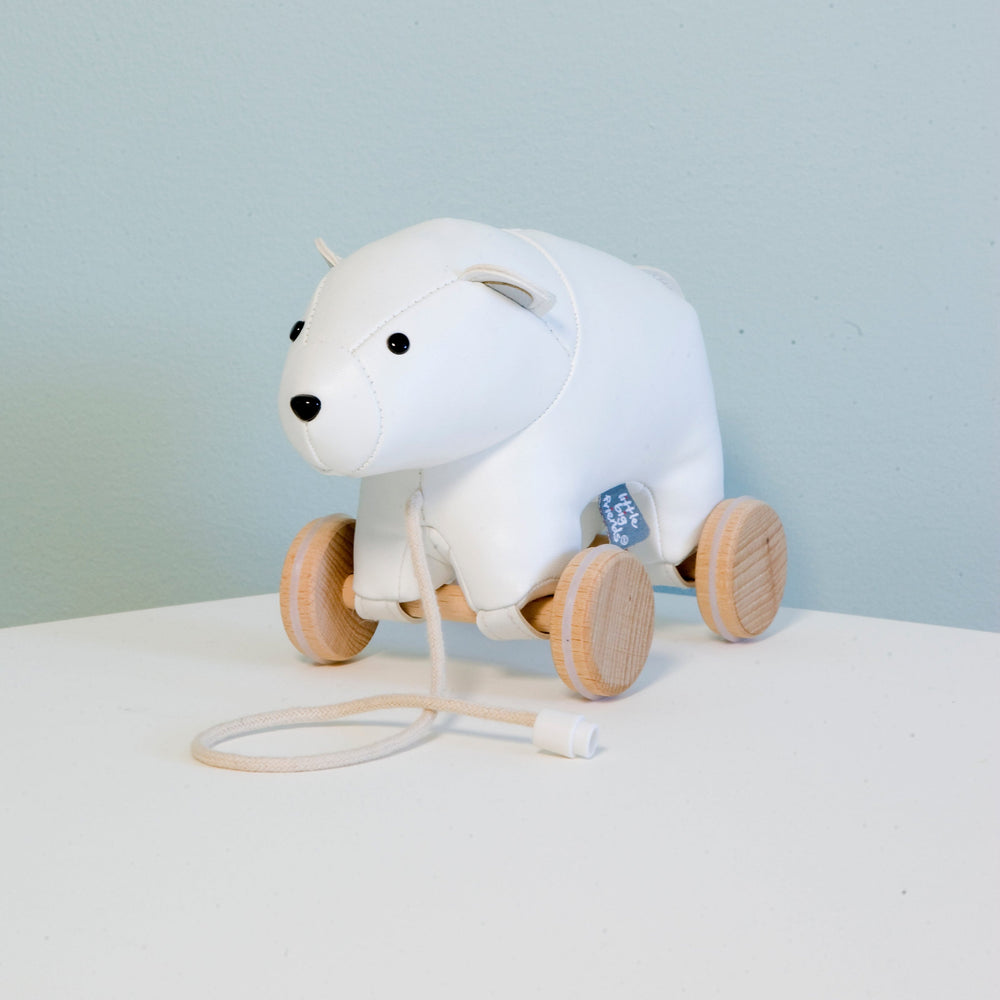White polar bear pull toy with wooden wheels on a light blue background