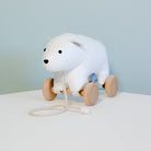 White polar bear pull toy with wooden wheels on a light blue background