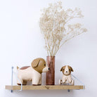 Two dog-shaped figurines on a shelf with a vase of dried flowers against a white background